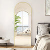 A full length arch mirror with a gold aluminum frame reflecting a bright interior and outdoor view.