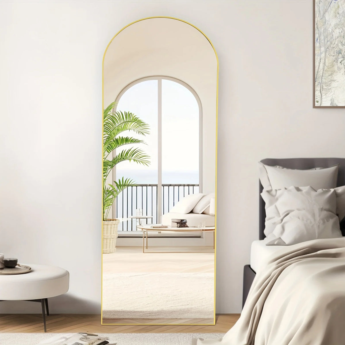 A full length arch mirror with a gold aluminum frame reflecting a bright interior and outdoor view.