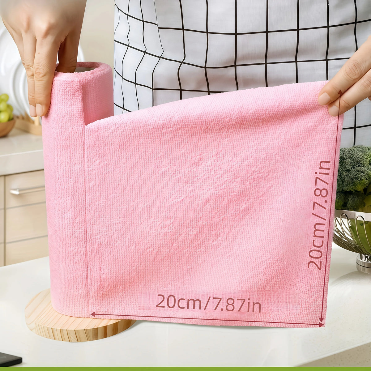 A hand holds a pink reusable microfiber cleaning cloth, measuring 20cm/7.87in, against a checkered background.