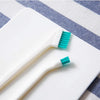 A white dual-sided silicone cleaning brush set with teal bristles resting on a striped cloth.