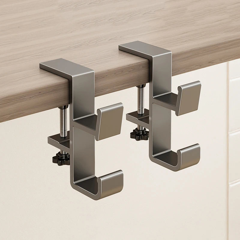 A close-up view of a metal adjustable desk hook bag hanger mounted on a wooden desk surface.