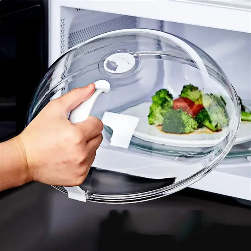 A hand is opening a transparent splash-proof oven cover with a white handle over a plate of food.