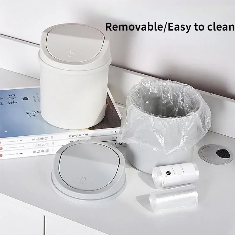 A white compact desktop trash can with a removable flip cover and related cleaning accessories are displayed on a white surfa
