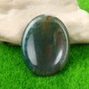 A polished green and brown natural quartz thumb stone resting on bright green grass.