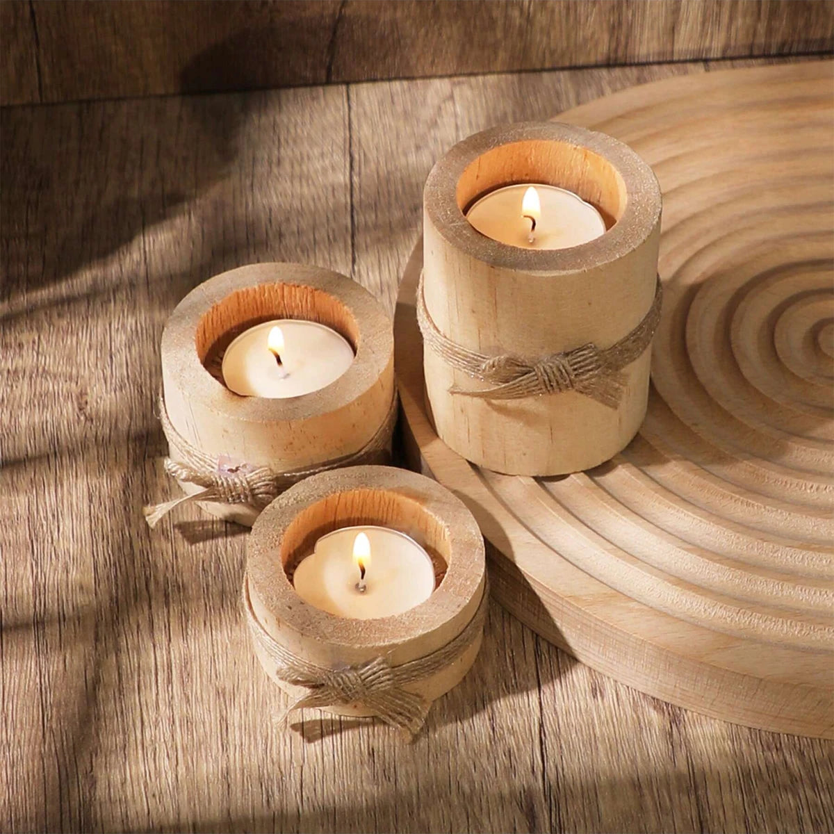 Tres portavelas de té de madera natural con velas encendidas, dispuestas sobre una superficie de madera clara.