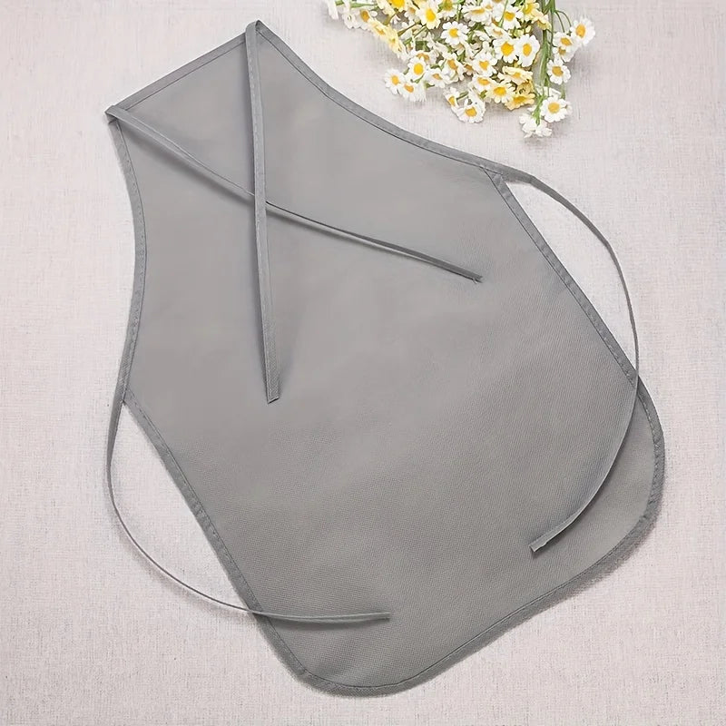 A light gray non-woven craft apron is displayed on a fabric background with a sprig of white and yellow flowers.