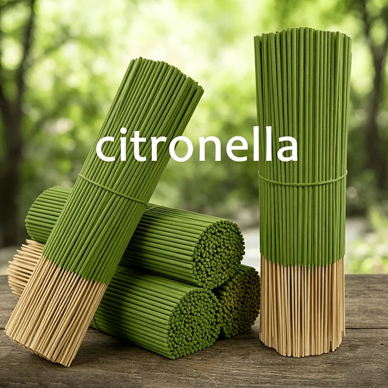 Green citronella oil sticks standing upright on a wooden surface with fresh greenery in the background.