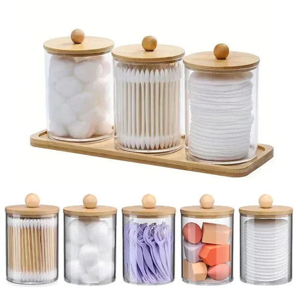 A set of glass apothecary jars with wooden lids filled with white and purple bath salts or similar granular products.