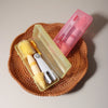 A silicone baby bottle cleaning set with pink and yellow brushes and a clear storage case resting on a woven mat.