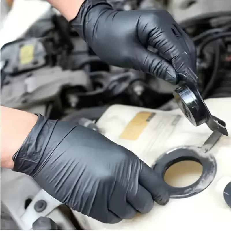 A hand wearing a black nitrile cleaning glove is holding a tool near a white surface.