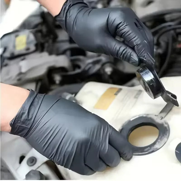 A hand wearing a black nitrile cleaning glove is holding a tool near a white surface.