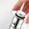 A hand is holding a stainless steel brass sink drain strainer with a removable filter.
