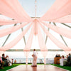 A wedding or event setup featuring sheer pink chiffon draping fabric suspended from a metal structure over an outdoor area.