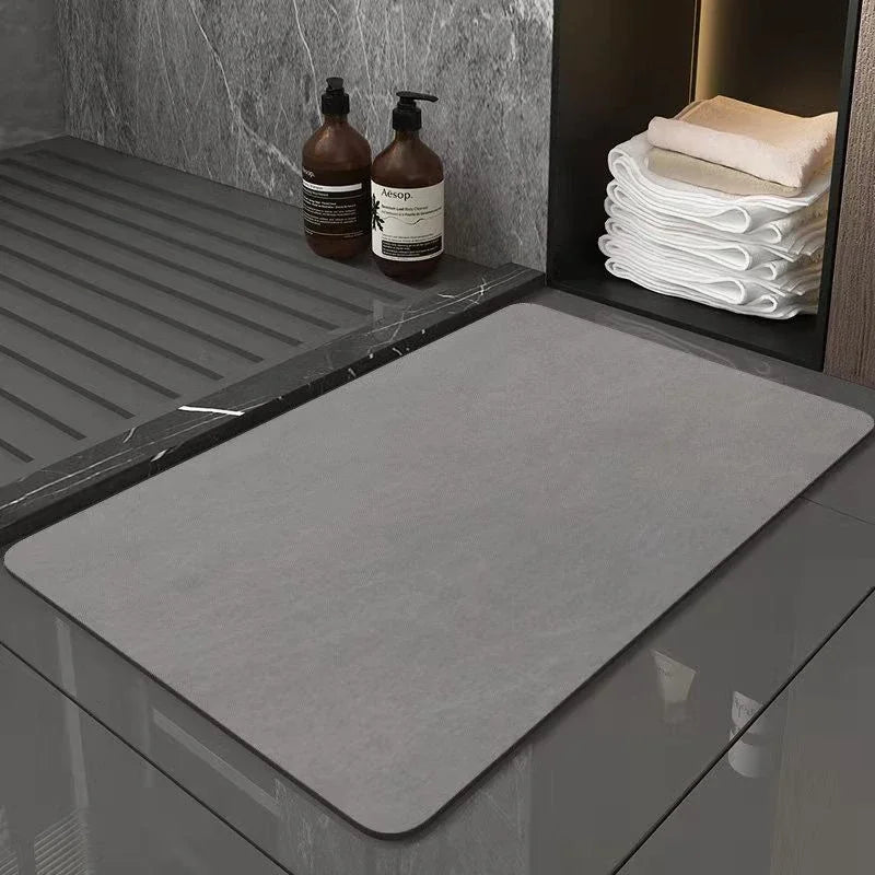 A gray diatomite eco-friendly non-slip bath mat placed on a dark marble surface next to soap bottles.