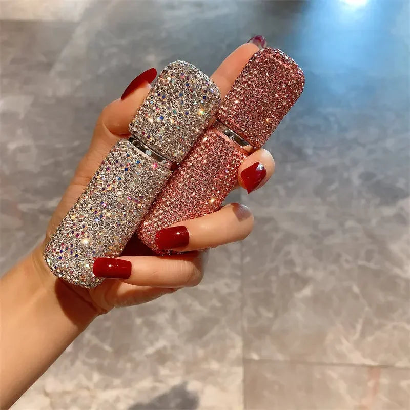 A hand holds three glittery pink and silver perfume spray bottles with red nail polish.