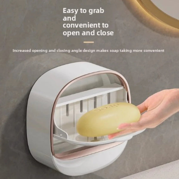 A hand is opening a wall-mounted soap holder with a lid to access the soap.