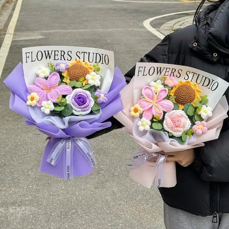 A bouquet of handmade crochet flowers in purple and pink hues is held by a person against an asphalt background.