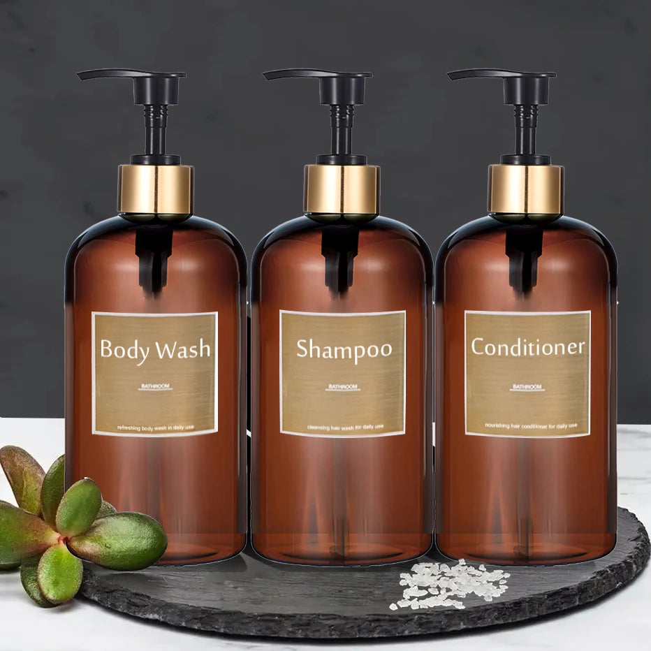 Three refillable pump soap dispenser bottles for body wash shampoo and conditioner displayed on a dark slate.