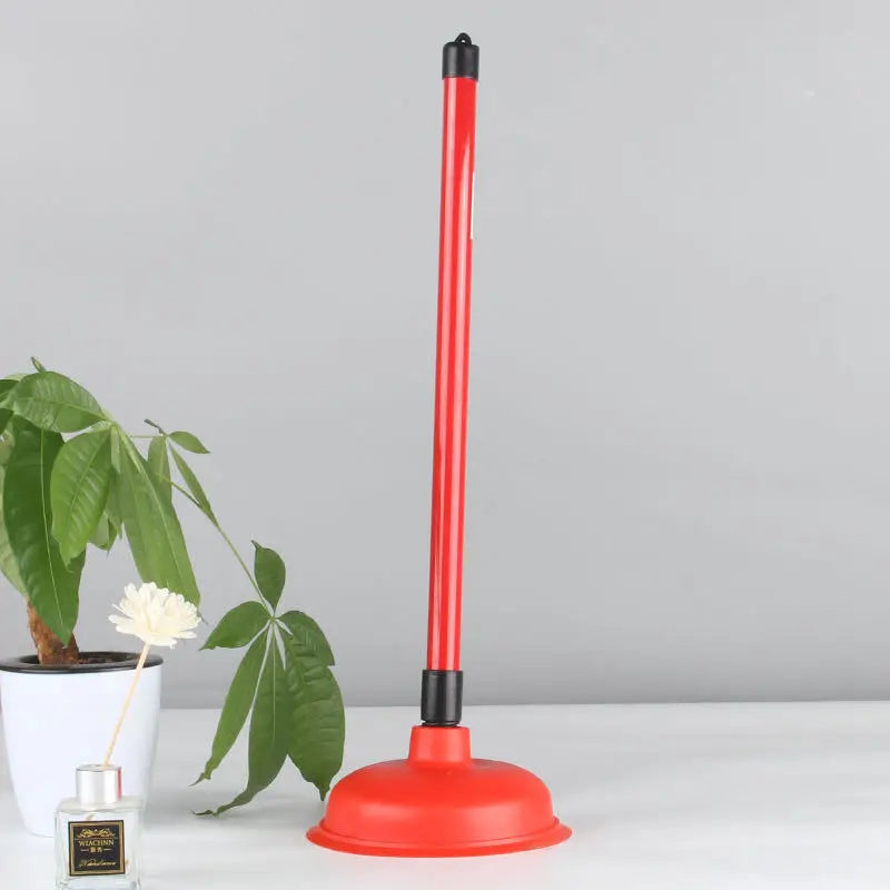 A red heavy-duty toilet plunger with a black handle and base standing on a white surface.