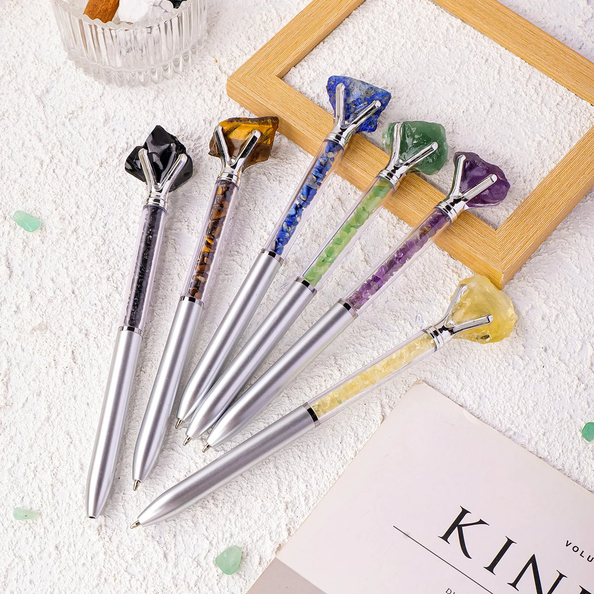 A collection of natural amethyst crystal pens with various colored crystals displayed on a white surface.