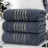 A stack of three dark gray bath towels with gold stripes resting on a white countertop.