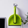 A bright lime green mini handheld dustpan and brush set resting on a white surface next to a tablet.