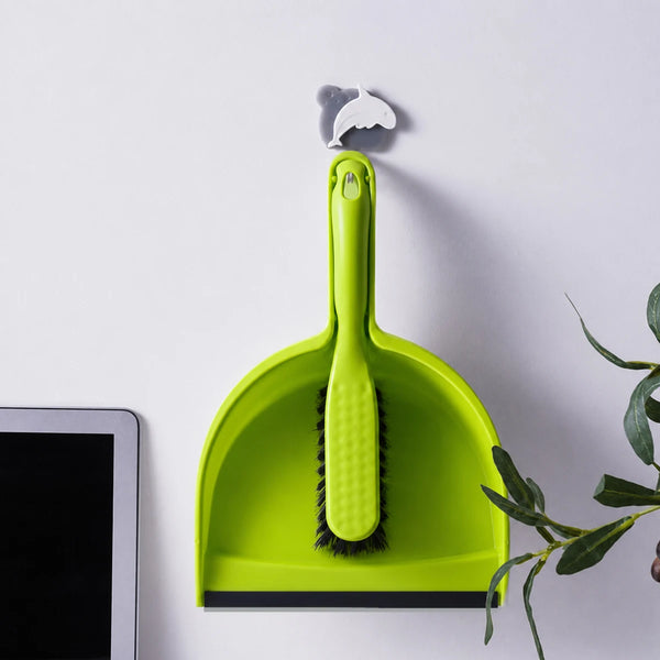 A bright lime green mini handheld dustpan and brush set resting on a white surface next to a tablet.