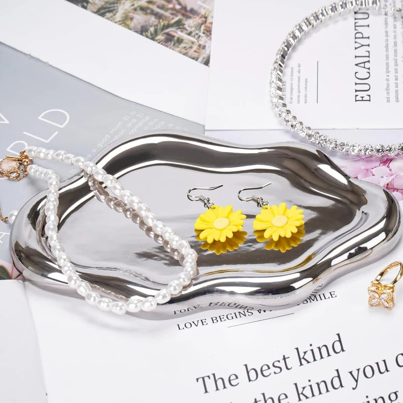A silver cloud-shaped jewelry organizer tray holding pearl and yellow floral earrings.