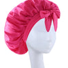 A vibrant pink silky satin sleep bonnet tied with a bow displayed on a white mannequin head.