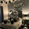 Decoración de cumpleaños con guirnalda de globos foil plateados y negros con el número 29 colgada sobre una cama.