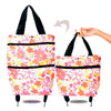A pink floral patterned foldable shopping bag with black handles and wheels.