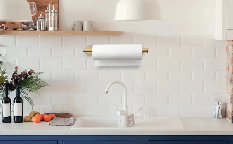 A stainless steel under cabinet paper towel holder mounted on a white tiled backsplash above a kitchen sink.