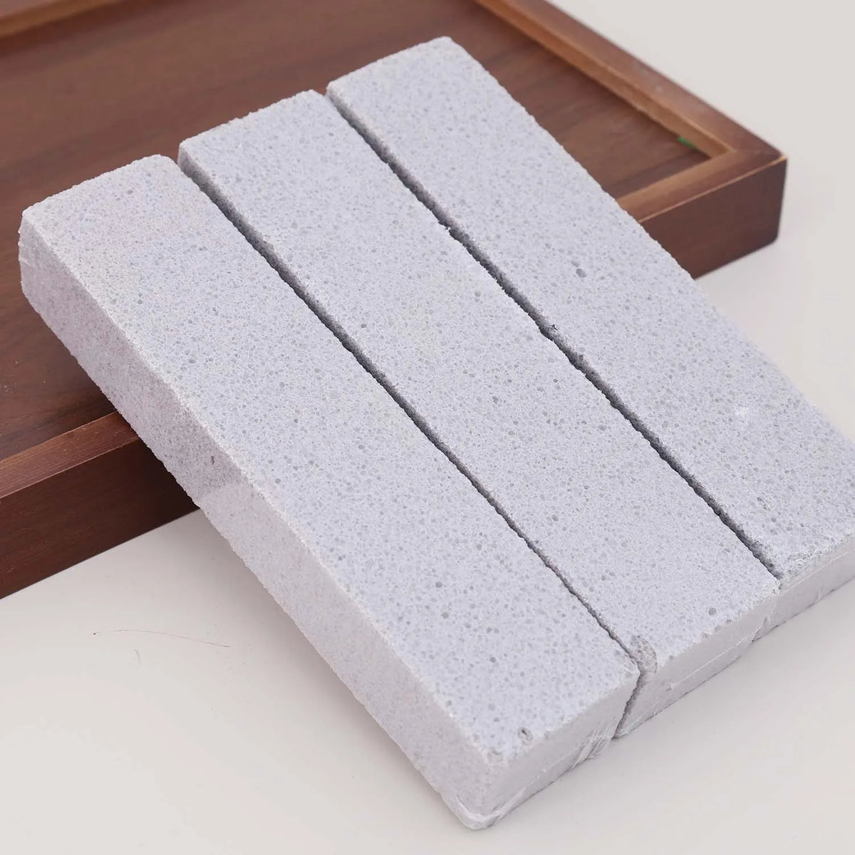 Three white pumice stones arranged diagonally on a wooden tray for stain removal.