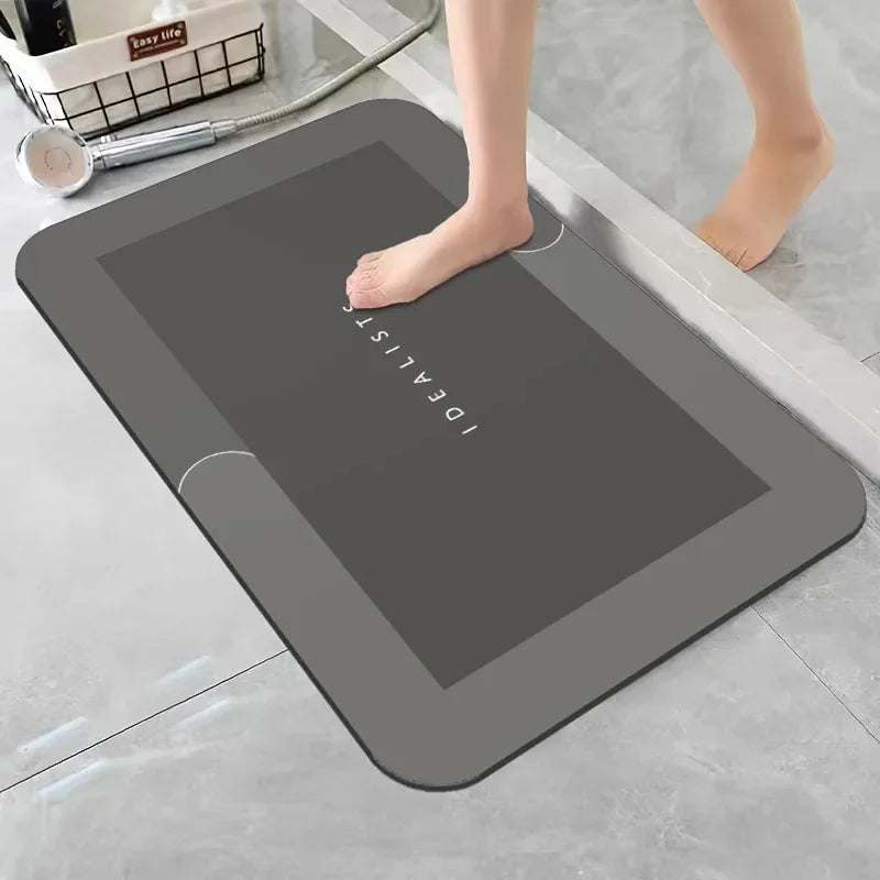 A gray diatomaceous earth absorbent bath mat is placed on a light-colored floor next to a person's foot.