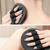 Eine Hand benutzt eine schwarze, gummiartige Body-Scrub- und Massagebürste auf der Haut eines Menschen im Nackenbereich.