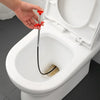 A hand is using a red and black sink and drain unclogging tool to clear a clog in a white toilet bowl.