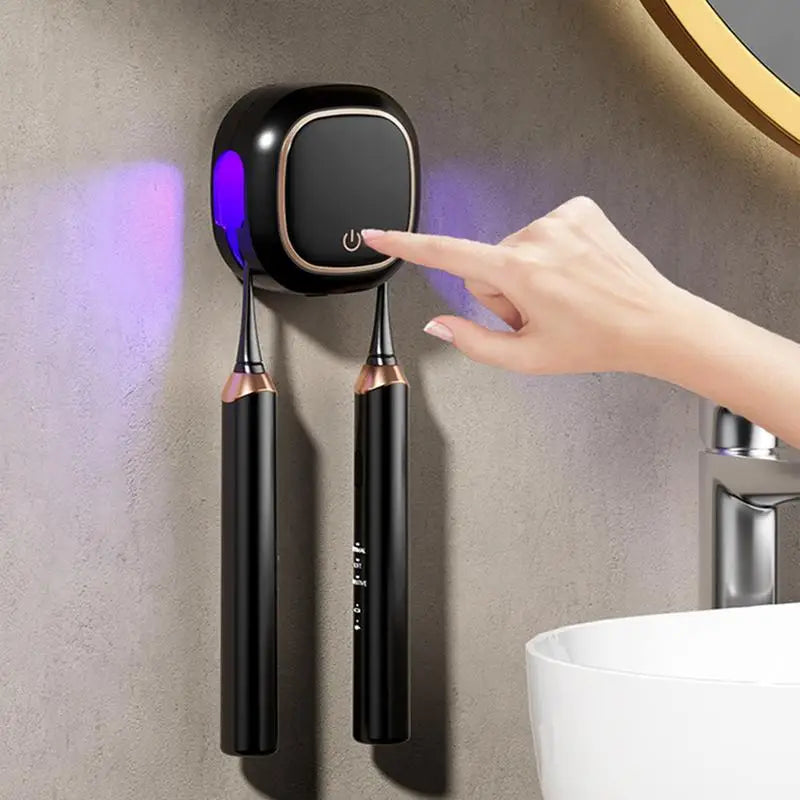 A hand is using a portable UV electric toothbrush cleaner device mounted on a wall above a sink.