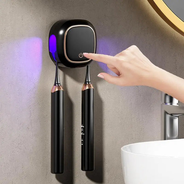 A hand is using a portable UV electric toothbrush cleaner device mounted on a wall above a sink.