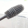 A silicone bottle brush with a long handle is shown dipping into a clear liquid.
