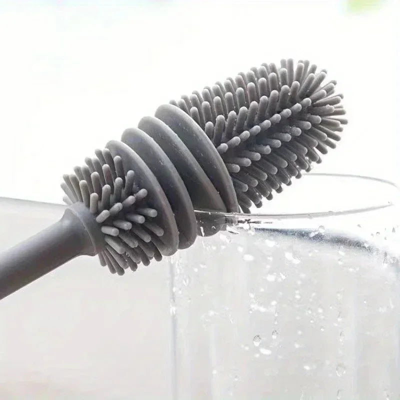 A silicone bottle brush with a long handle is shown dipping into a clear liquid.