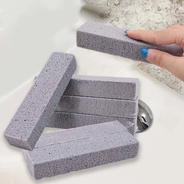A hand is holding a gray pumice stone used for stain removal, with several stones visible on a white surface.