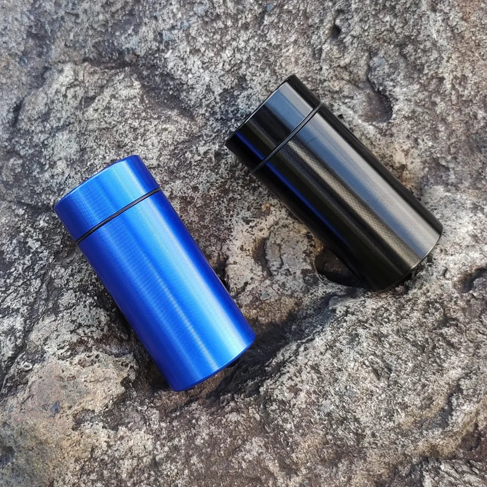 A pair of black and blue airtight aluminum stash jars resting on a rough gray stone surface.