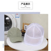 A white mesh reusable laundry bag is displayed on a white surface next to a green baseball cap.