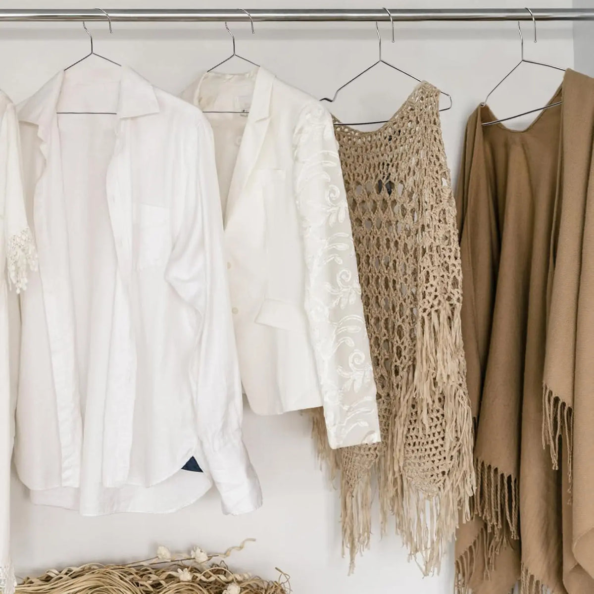 A display of various light-colored and beige knitted sweaters and jackets hanging on a metal rack.