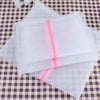 A stack of white mesh laundry bags with pink zippers resting on a checkered cloth.