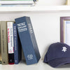 A dark blue hardcover dictionary titled The New English Dictionary sits next to a dark blue cap on a white shelf.