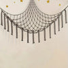 A decorative netting hammock with fringe and gold stars hangs against a light wall.