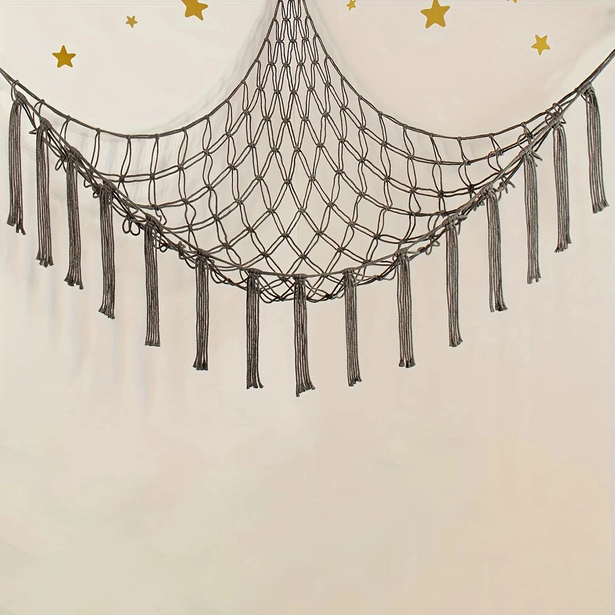 A decorative netting hammock with fringe and gold stars hangs against a light wall.