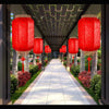 A row of red Chinese lanterns hangs from a pergola walkway lined with greenery and stone pillars.