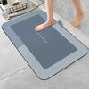 A gray diatomaceous earth absorbent bath mat is placed on a light gray floor next to a person's bare foot.
